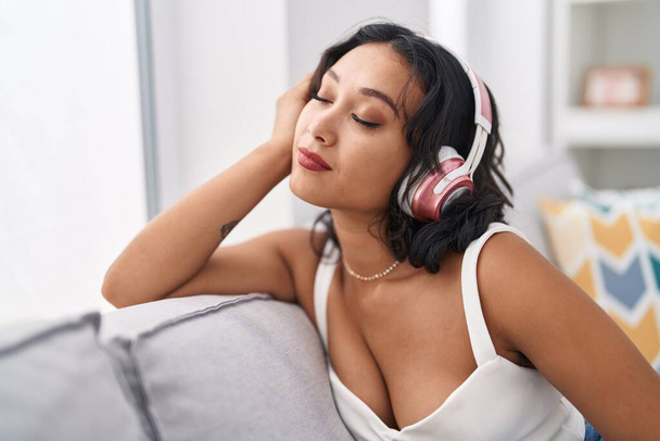 Nuori kaunis latino nainen kuuntelee musiikkia rento sohvalla kotona - Valokuva, kuva