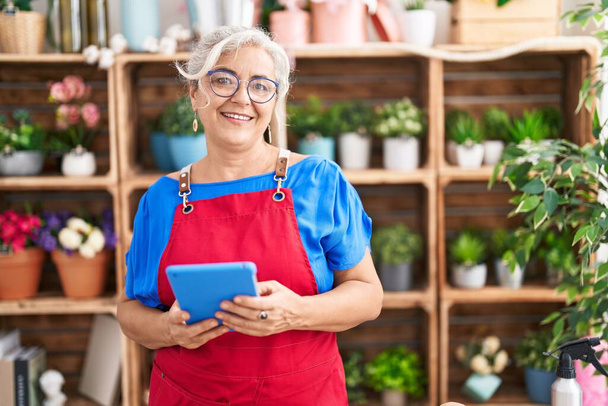 Middle age grey-haired woman florist smiling confident using touchpad at florist - Photo, Image