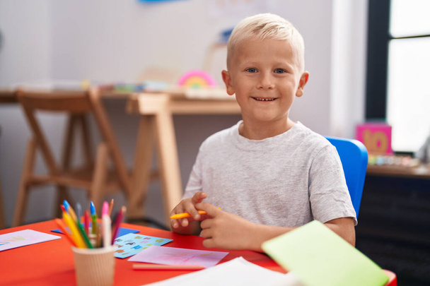Little caucasian boy painting at the school looking positive and happy standing and smiling with a confident smile showing teeth  - 写真・画像