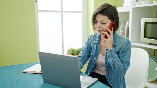 Giovane donna caucasica che parla su smartphone utilizzando il computer portatile a casa - Foto, immagini