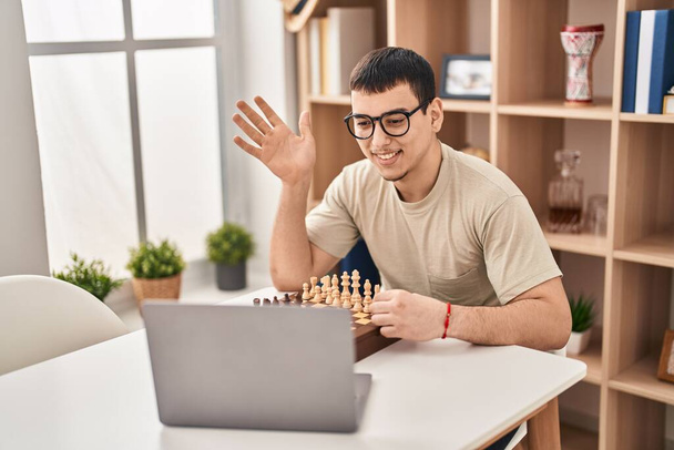Hombre árabe joven jugando ajedrez en línea celebrando logro con sonrisa feliz y expresión ganadora con la mano levantada  - Foto, Imagen