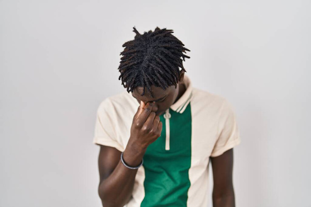 African man with dreadlocks standing over isolated background tired rubbing nose and eyes feeling fatigue and headache. stress and frustration concept.  - Foto, imagen