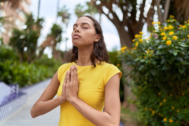 Giovane donna afroamericana che prega con gli occhi chiusi al parco - Foto, immagini