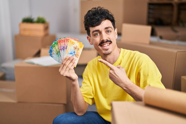 Hispanischer Mann im neuen Zuhause mit Schweizer Franken-Banknoten in der Hand lächelnd glücklich mit Hand und Finger zeigend  - Foto, Bild