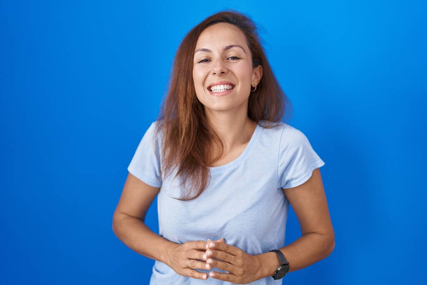 Brunette woman standing over blue background hands together and fingers crossed smiling relaxed and cheerful. success and optimistic  - Photo, Image
