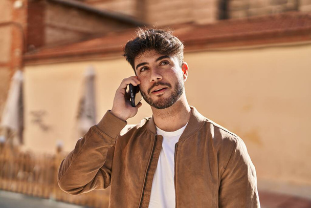 Joven hombre hispano sonriendo confiado hablando en el teléfono inteligente en la calle - Foto, imagen