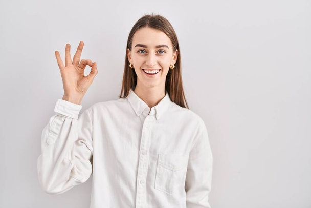Young caucasian woman standing over isolated background smiling positive doing ok sign with hand and fingers. successful expression.  - Photo, Image