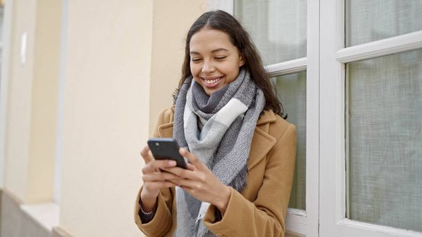 Mujer hispana hermosa joven usando teléfono inteligente sonriendo en la calle - Foto, imagen