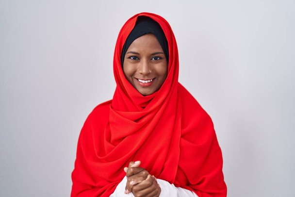 Jonge Arabische vrouw draagt traditionele islamitische hijab sjaal met handen bij elkaar en gekruiste vingers glimlachend ontspannen en vrolijk. succes en optimisme  - Foto, afbeelding