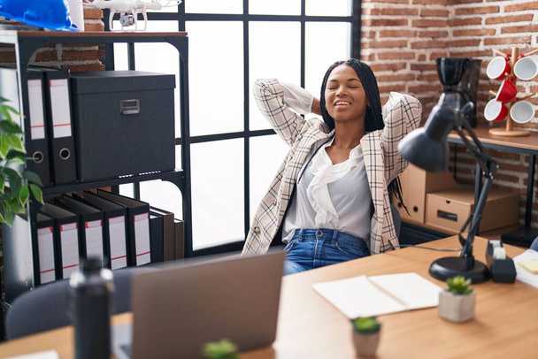 Африканская американка бизнес-работница расслабленная с руками на голове в офисе - Фото, изображение