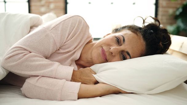 Middle age hispanic woman smiling confident lying on bed at bedroom - Foto, imagen