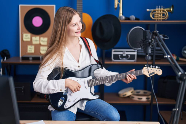 Young caucasian woman artist smiling confident playing electrical guitar at music studio - Fotó, kép