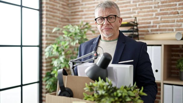 Hombre de pelo gris de mediana edad trabajador de negocios despedido holding caja de cartón en la oficina - Foto, Imagen