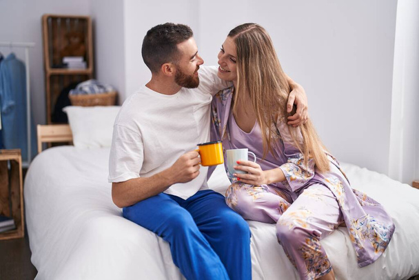 Man and woman couple hugging each other drinking coffee at bedroom - Photo, image