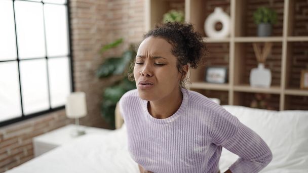 African american woman suffering for stomach ache sitting on bed at bedroom - Foto, immagini