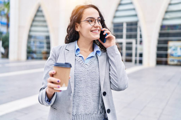 Young hispanic woman executive drinking coffee talking on the smartphone at street - Photo, Image