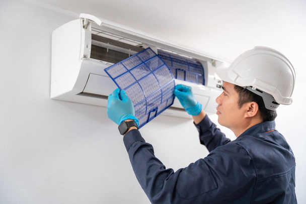 エアコン技術者は、白い壁にエアコンのほこりをきれいにするために空気フィルターを削除します. - 写真・画像