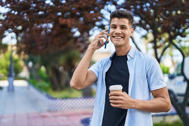 Jovem hispânico falando no smartphone bebendo café no parque - Foto, Imagem