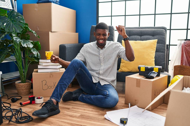 Αφροαμερικάνος που κάθεται στο πάτωμα στο νέο σπίτι χορεύοντας χαρούμενος και χαρούμενος, χαμογελαστός συγκινητικός χαλαρός και σίγουρος ακούγοντας μουσική  - Φωτογραφία, εικόνα