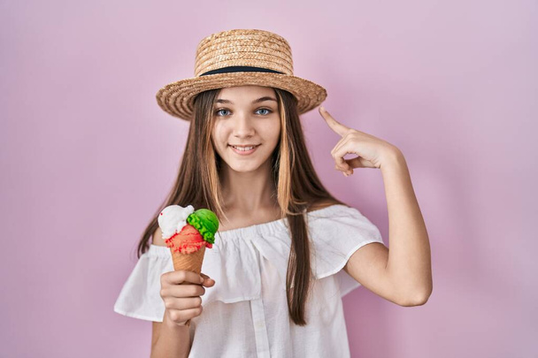 Dondurma tutan genç kız tek parmakla kafasını işaret ediyor, harika bir fikir ya da düşünce, iyi hafıza  - Fotoğraf, Görsel