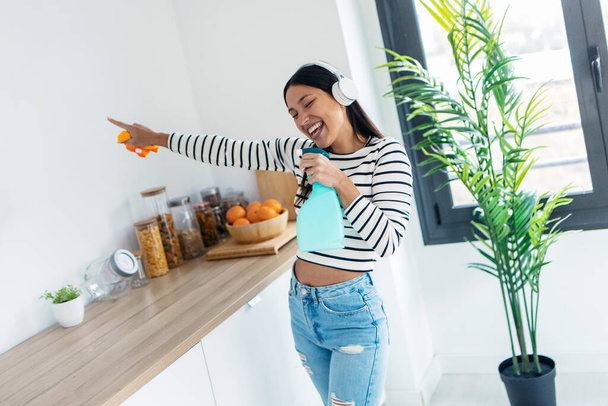 Tiro de bela mulher feliz cantando e dançando enquanto limpa a cozinha em casa - Foto, Imagem