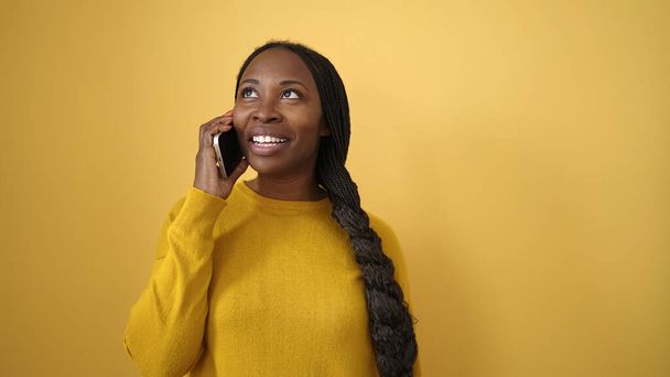 Femme africaine souriante parlant au téléphone sur fond jaune isolé - Photo, image
