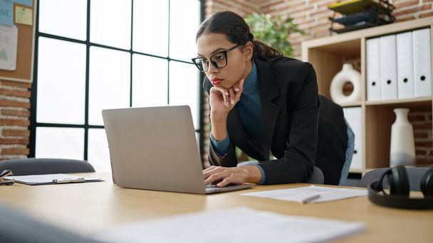 Giovane bella donna ispanica business worker utilizzando computer portatile in piedi in ufficio - Foto, immagini