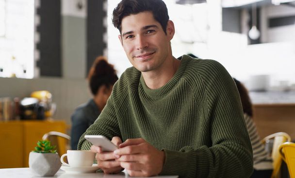 You have a whole big world to connect with. Portrait of a handsome young man using a cellphone in a cafe - Foto, Imagen