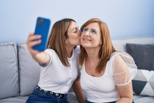 Mother and daughter making selfie by the smartphone sitting on sofa at home - Zdjęcie, obraz