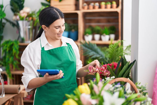 Young beautiful hispanic woman florist smiling confident using touchpad at flower shop - Zdjęcie, obraz