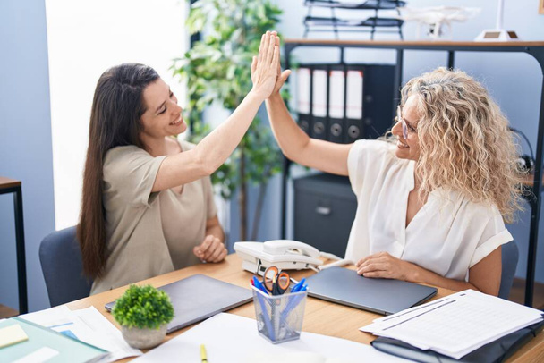 Две женщины-предпринимательницы "дай пять" с поднятыми руками в офисе - Фото, изображение