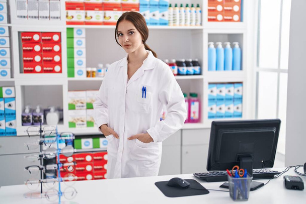 Young woman pharmacist smiling confident standing at pharmacy - 写真・画像