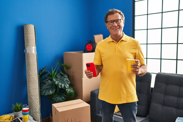 Hombre de mediana edad usando teléfono inteligente beber café en un nuevo hogar - Foto, imagen