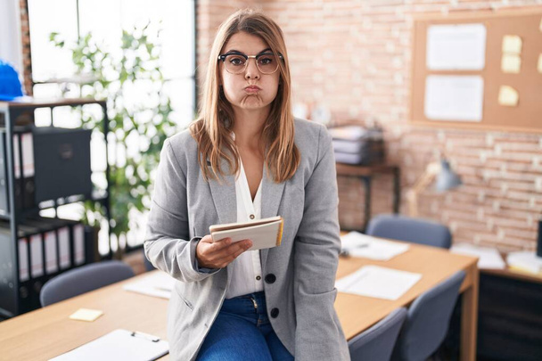 Молода іспаномовна жінка працює в офісі в окулярах, набиваючи щоки смішним обличчям. рот надутий повітрям, божевільний вираз
.  - Фото, зображення