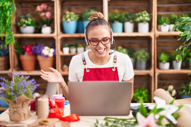 Young hispanic woman working at florist shop doing video call celebrating achievement with happy smile and winner expression with raised hand  - Fotó, kép