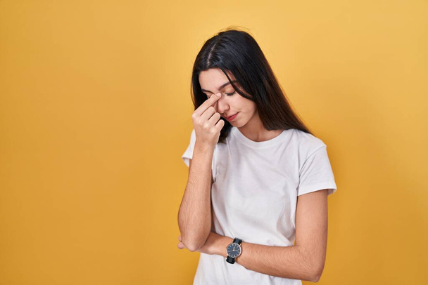 Young beautiful woman standing over yellow background tired rubbing nose and eyes feeling fatigue and headache. stress and frustration concept.  - Photo, image