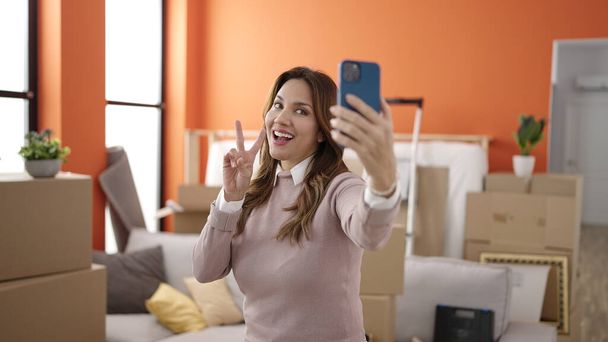 Junge schöne hispanische Frau lächelt selbstbewusst Selfie mit dem Smartphone im neuen Zuhause - Foto, Bild