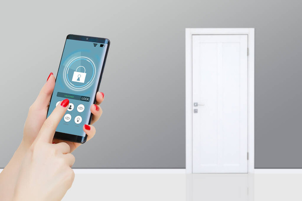 Female hand holding black mobile smart phone with smart home application on the screen. Blurred house on the background. For access to all of the controls of your house and caring of home security. - Photo, Image