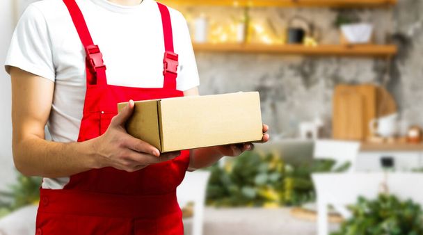 Junger lächelnder Logistiker in roter Uniform hält die Schachtel. - Foto, Bild