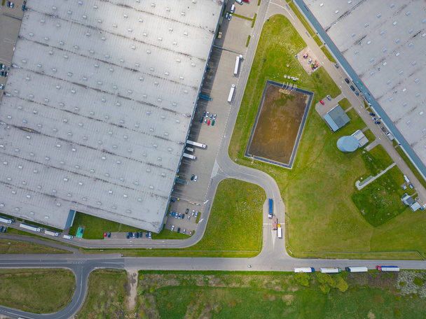 Aerial view of goods warehouse. Logistics center in industrial city zone from above. Aerial view of trucks loading at logistic center - Фото, изображение