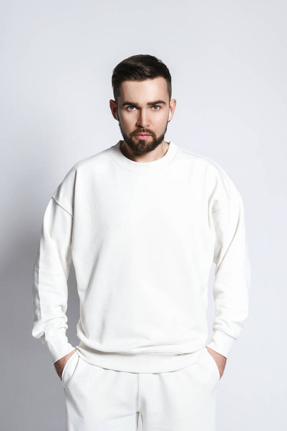 Handsome man wearing white sweatshirt with wireless earbuds against gray background - Foto, Imagen