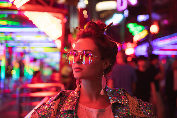 Young stylish woman wearing jacket with shining sequins on the city street with neon lights - Photo, Image