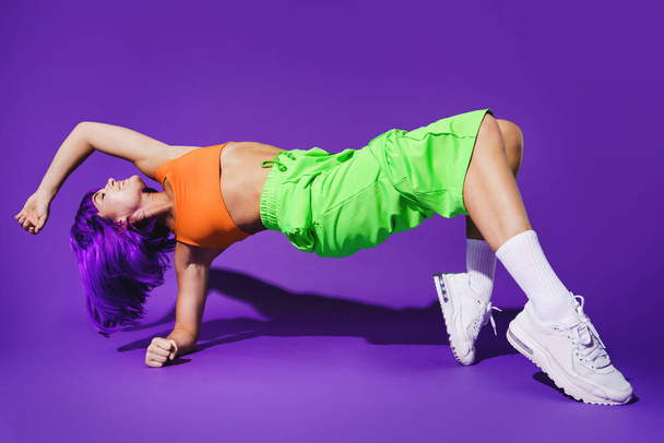 Carefree active woman dancer wearing colorful sportswear performing against purple background - Photo, image