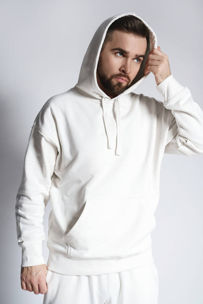 Handsome man wearing blank white hoodie and pants posing on gray background - Fotó, kép