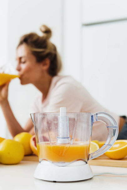 Крупним планом цитрусовий соковижималка і жінка, які п'ють свіжовичавлений домашній апельсиновий сік
  - Фото, зображення