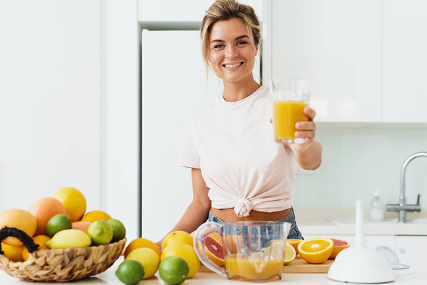 Young cheerful woman with big glass of fresh orange juice at home - Foto, Bild