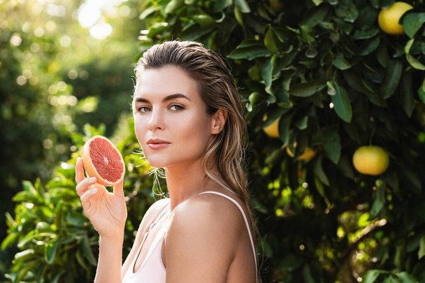 Outdoor portrait of beautiful woman with smooth skin with a grapefruit in her hands - Fotó, kép