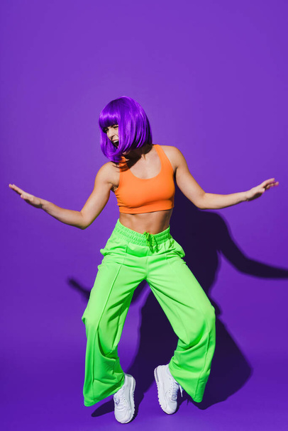 Carefree active woman dancer wearing colorful sportswear having fun against purple background - Фото, изображение