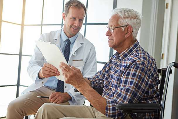 Going through his medical chart. a male doctor talking to a senior patient in the retirement home - Foto, imagen