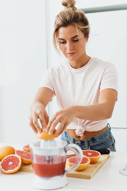 Young woman with a lot of citrus fruits during fresh grapefruit juice preparation at home - Fotó, kép